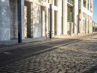 a street with a bike on the sidewalk in front of a building with windows and a woman in the foreground