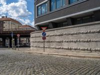 a cobblestone street next to two buildings with street signs on them, on a partly cloudy day