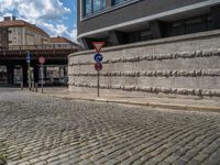 a cobblestone street next to two buildings with street signs on them, on a partly cloudy day