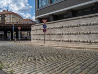 a cobblestone street next to two buildings with street signs on them, on a partly cloudy day