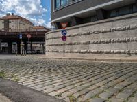 a cobblestone street next to two buildings with street signs on them, on a partly cloudy day