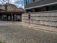 a cobblestone street next to two buildings with street signs on them, on a partly cloudy day