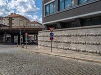 a cobblestone street next to two buildings with street signs on them, on a partly cloudy day