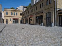 the sidewalk is paved with stones and has a bench in front of it, with no people inside