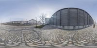 a 360 camera is pointed at a curved building with a circular entrance, in the middle of a cobblestone plaza