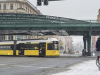 a cyclist riding on the road near a bus and cars on the street below an elevated railway