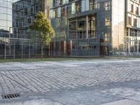 an empty paved square sits on a sidewalk in front of large buildings with glass facades