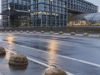 several concrete spheres in the rain and on an empty street with buildings in the background