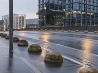 several concrete spheres in the rain and on an empty street with buildings in the background