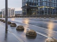 several concrete spheres in the rain and on an empty street with buildings in the background