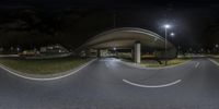 a curved overpass over an empty city road at night with street lights and grass