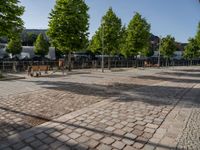 an empty city square with lots of benches and trees on either side of the brick pavement