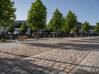 an empty city square with lots of benches and trees on either side of the brick pavement