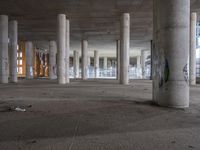 a empty parking garage filled with graffiti and a bunch of columns in it by some buildings