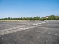 an empty parking lot with a sky background and trees lining the lot with houses behind