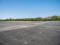 an empty parking lot with a sky background and trees lining the lot with houses behind