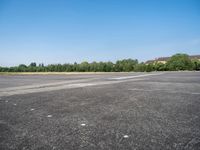 an empty parking lot with a sky background and trees lining the lot with houses behind