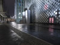 a street and some very tall buildings at night - colored lights in the dark and wet wet surface