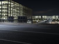 a car drives down the road beside a glass building at night with lights on it