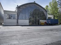 a large glass building in the background and trucks parked at the side of it to the right