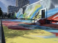 the entrance of a graffiti covered warehouse building with a skate ramp painted on it, there are other buildings in the background