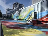 the entrance of a graffiti covered warehouse building with a skate ramp painted on it, there are other buildings in the background