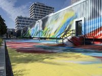 the entrance of a graffiti covered warehouse building with a skate ramp painted on it, there are other buildings in the background