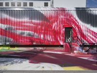 a red white and black and red painting on the wall of a building on the side walk