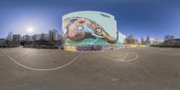 fish eye view of a graffiti covered building and a circular mural on the side of the building