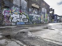 the graffiti is on the side of a building next to an alleyway with cement and broken puddles