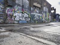 the graffiti is on the side of a building next to an alleyway with cement and broken puddles