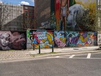 a wall with different colorful artwork on it in a city with buildings around and the street has a bike path going under it