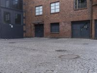 brick patio next to building with large doors near windows with no people on it and an empty space between two buildings