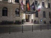 the entrance to an hotel has multiple flags outside of it and street lights on both sides