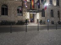 the entrance to an hotel has multiple flags outside of it and street lights on both sides