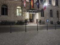 the entrance to an hotel has multiple flags outside of it and street lights on both sides