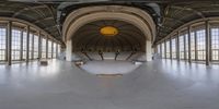 a large open indoor area with many windows and concrete steps, with skateboard ramp in foreground