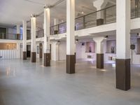 large room with lights, furniture and white walls and cement flooring with columns and staircase