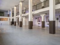 large room with lights, furniture and white walls and cement flooring with columns and staircase