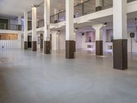 large room with lights, furniture and white walls and cement flooring with columns and staircase