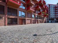 the cobblestone street in front of an apartment complex has red balconies with a lamp post