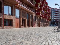 the cobblestone street in front of an apartment complex has red balconies with a lamp post