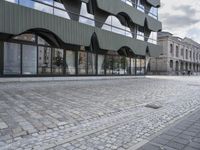 an empty sidewalk leading to a building with windows that look like fish scales and curved waves