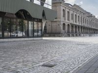 an empty sidewalk leading to a building with windows that look like fish scales and curved waves