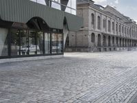 an empty sidewalk leading to a building with windows that look like fish scales and curved waves