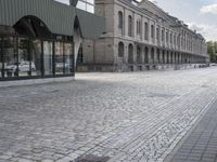 an empty sidewalk leading to a building with windows that look like fish scales and curved waves