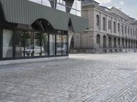 an empty sidewalk leading to a building with windows that look like fish scales and curved waves