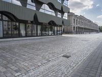 an empty sidewalk leading to a building with windows that look like fish scales and curved waves