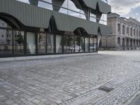 an empty sidewalk leading to a building with windows that look like fish scales and curved waves