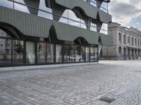 an empty sidewalk leading to a building with windows that look like fish scales and curved waves